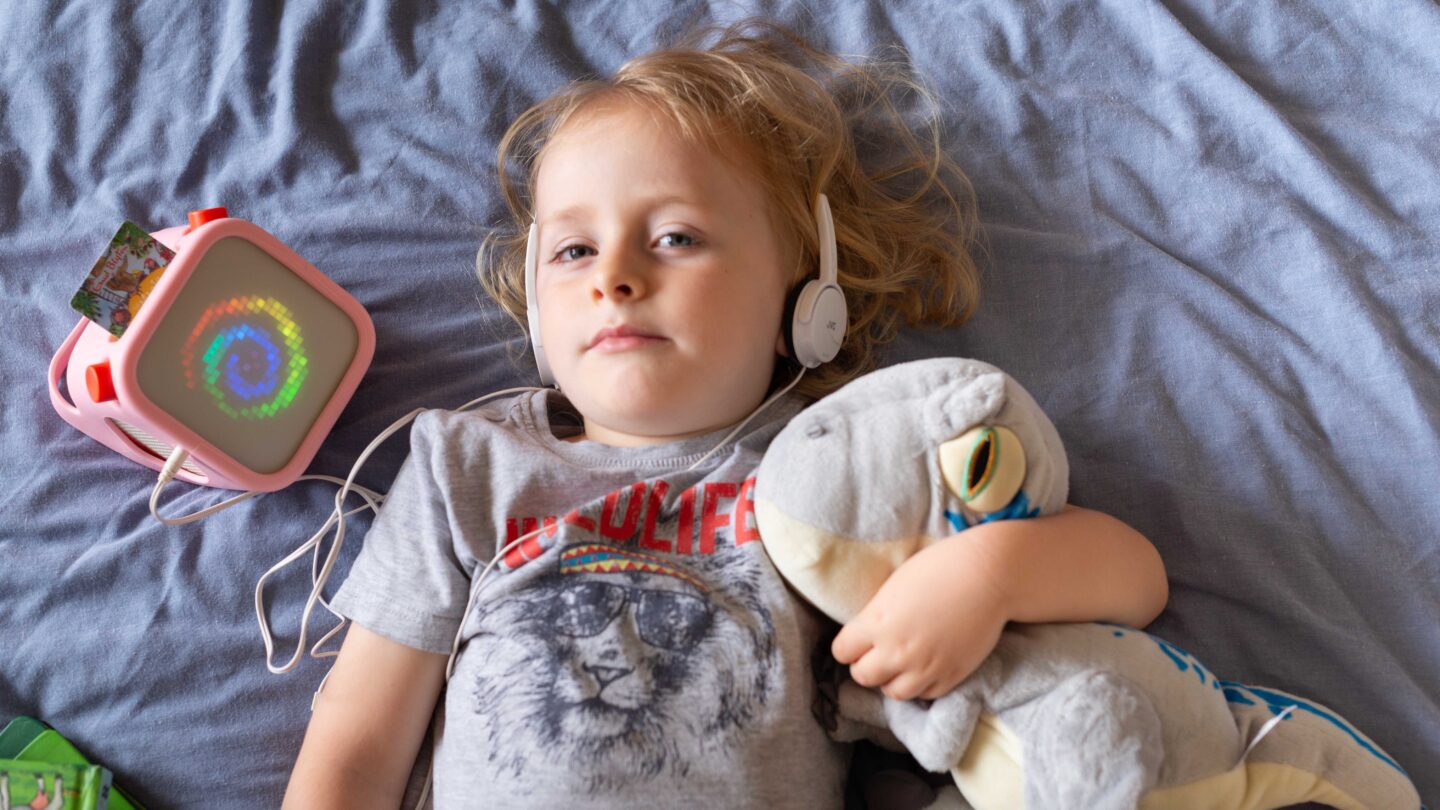 Young child listening to Yoto Player 3rd Generation audiobook with headphones.